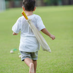 A child playing with a the PlanToys Mini Golf Set outside on grass. He is running towards the ball on the ground with the canvas bag containing the clubs on his back. 