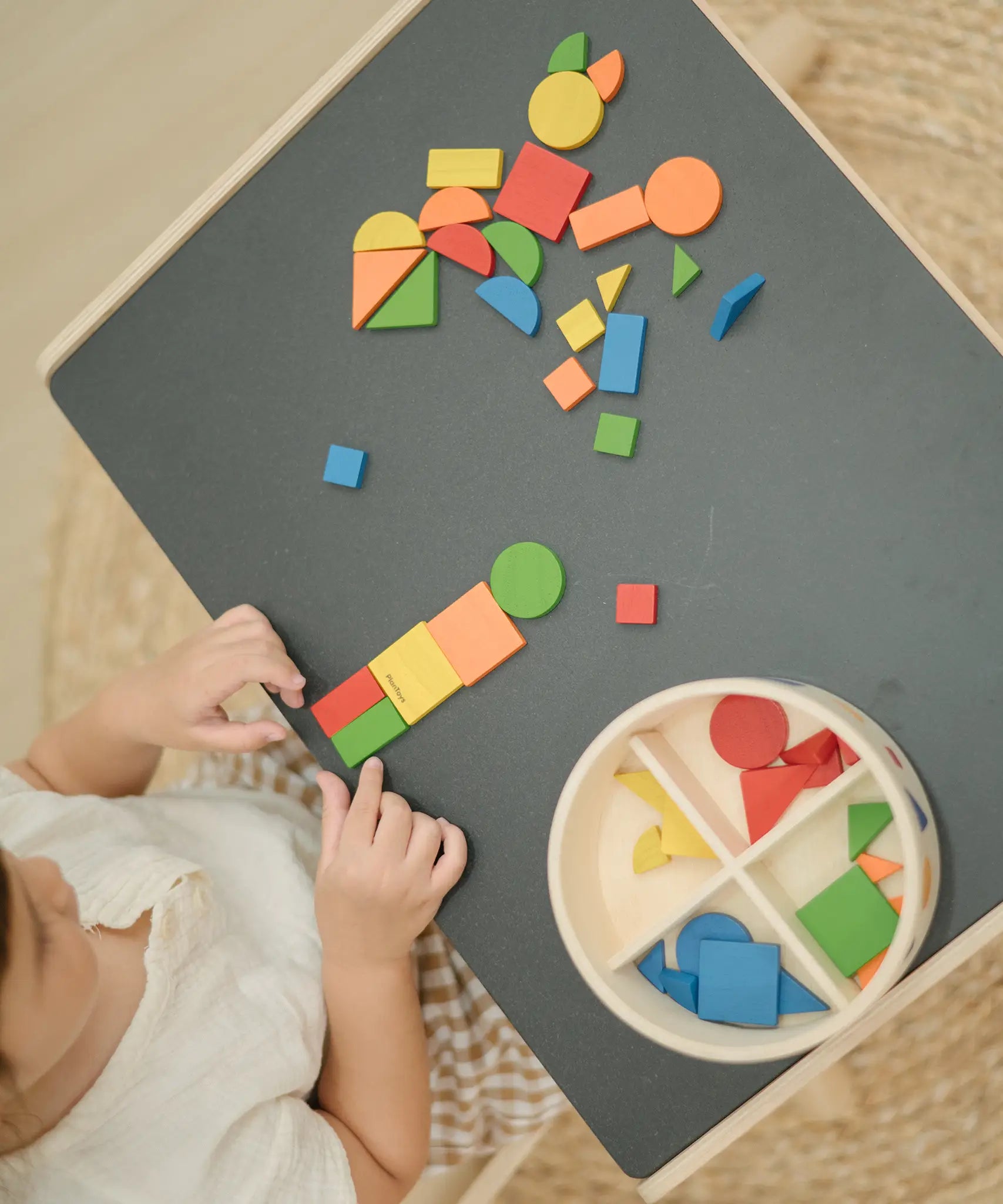 Overhead view of a child creating a colourful pattern using the wooden pieces from the PlanToys Mosaic wooden pattern making toy.