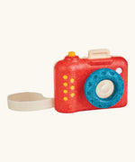 PlanToys my first wooden camera with a red body and blue lens. Features a working shutter button and cotton carry loop