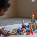 A child playing sitting on a rug playing with the PlanToys Castle Building Blocks set. 
