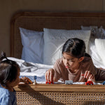 Two children playing with the PlanToys Mini Cars Set. One child is laying on a bed the other is standing up at the end of the bed.
