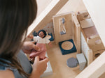 A child holding a wooden dolly, the PlanToys Bathroom Dolls House Furniture can be seen in the background.