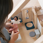 A child holding a wooden dolly, the PlanToys Bathroom Dolls House Furniture can be seen in the background.