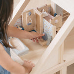 A child playing with the PlanToys Bathroom Dolls House Furniture that has been set up in a wooden dolls house.