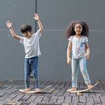 Two children, each standing upon a PlanToys Balance Board.