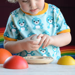 A child playing with the PlanToys Chicken Nesting Toy. The pieces have all been taken off the wooden bas and the child is holding on to the egg.
