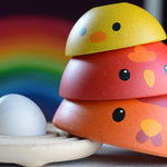 A close up of the A child playing with the PlanToys Chicken Nesting Toy. The egg has been placed on the wooden base with the three wooden chickens stacked up besides the base. 