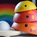 A close up of the A child playing with the PlanToys Chicken Nesting Toy. The egg has been placed on the wooden base with the three wooden chickens stacked up besides the base. 