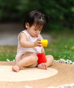 Child playing with the PlanToys Nesting Cylinders 3 piece wooden toy. Red, yellow and blue coloured wooden cylinder shaped wooden pieces that nest inside each other. 