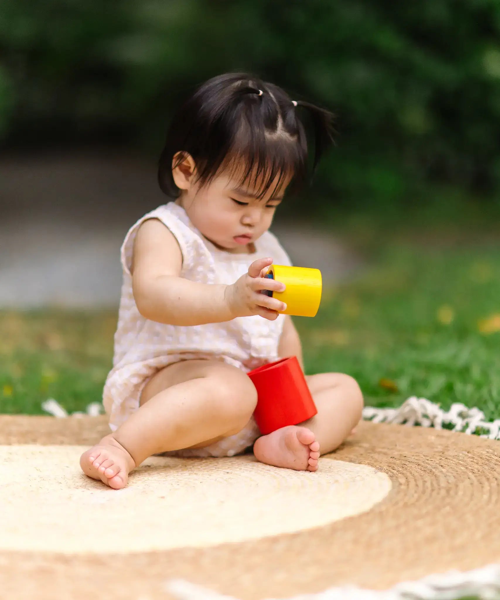 Child playing with the PlanToys Nesting Cylinders 3 piece wooden toy. Red, yellow and blue coloured wooden cylinder shaped wooden pieces that nest inside each other. 