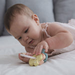 A baby laying on their tummy playing with the PlanToys Pastel Baby Key Rattle. 