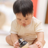 A baby sitting leaning towards the PlanToys Penguin Wobbler wooden baby toy. A circular shaped penguin toy that wobbles when placed on a flat surface. PlanToys range of toys are made from sustainably sourced rubberwood, we're proud stockists of PlanToys here at Babipur. 