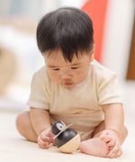 A baby sitting leaning towards the PlanToys Penguin Wobbler wooden baby toy. A circular shaped penguin toy that wobbles when placed on a flat surface. PlanToys range of toys are made from sustainably sourced rubberwood, we're proud stockists of PlanToys here at Babipur. 