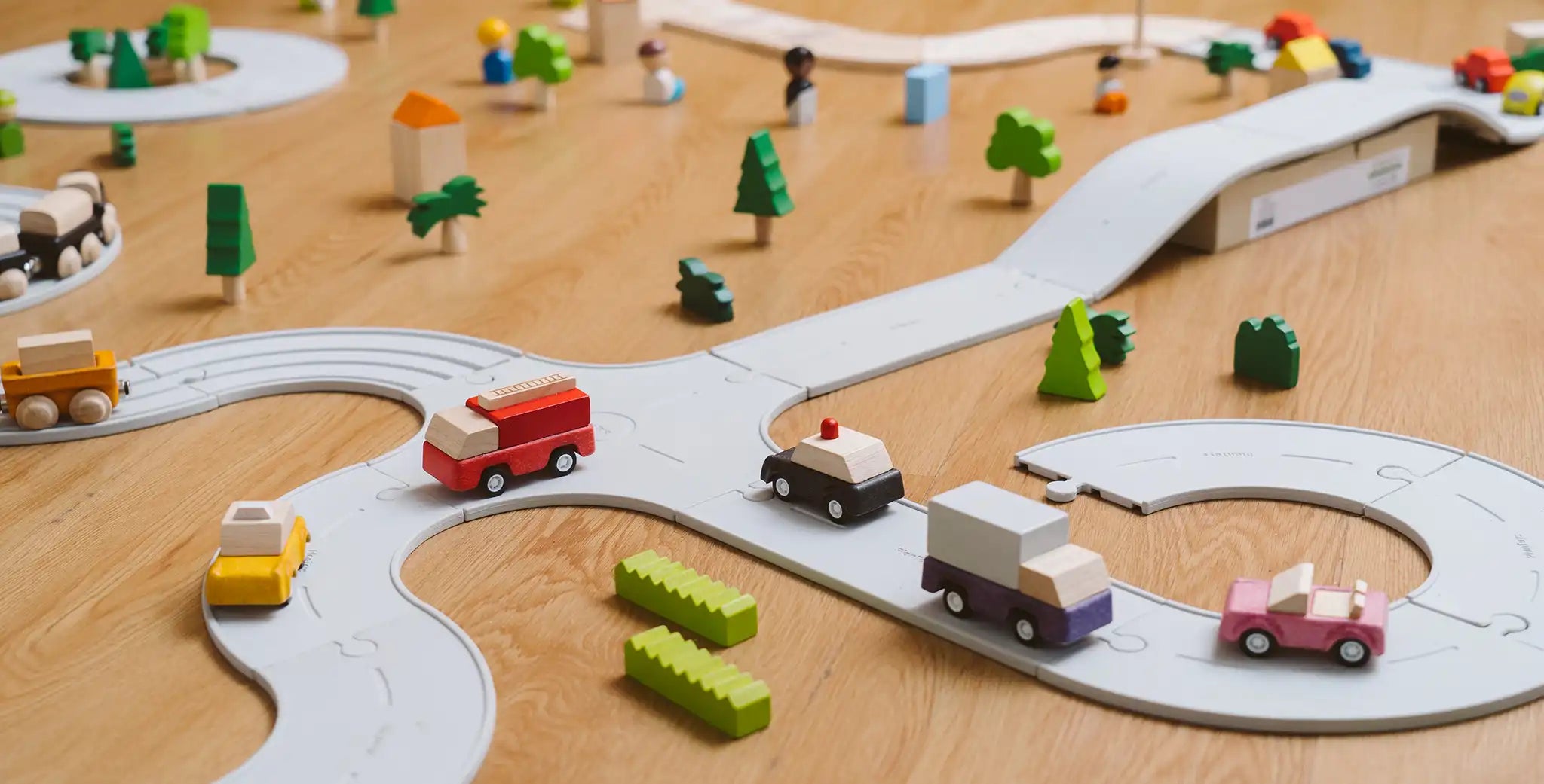 PlanToys PlanWorld vehicle wooden toy vehicles set shown on the rubber road. Red fire engine, purple truck, yellow taxi, pink convertible and black police car.