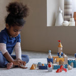 A child playing sitting on a rug playing with the PlanToys Castle Building Blocks set. 
