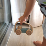 Close up of a childs hand picking up the Plan Toys eco-friendly vroom car pushing toy on a light wooden floor