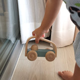 Close up of a childs hand picking up the Plan Toys eco-friendly vroom car pushing toy on a light wooden floor