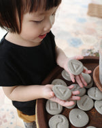 Girl tracing around the carvings in the Plan Toys wooden tactile stones on a dark brown table