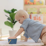 Baby playing with the PlanToys pop and drop wooden bucket baby posting toy placing the lid back on the top.