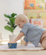 Baby playing with the PlanToys pop and drop wooden bucket baby posting toy placing the lid back on the top.