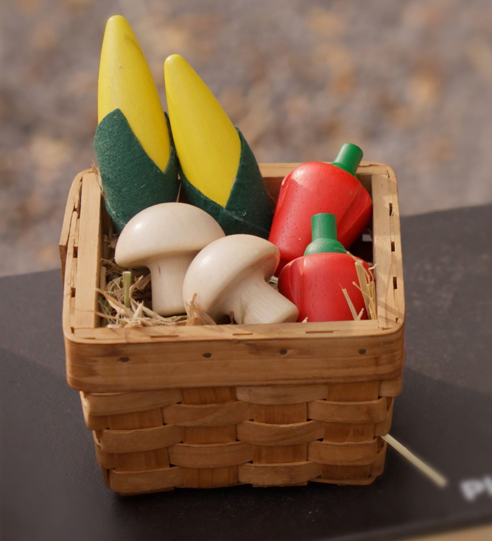 Plan Toys Wooden Produce Set - play food vegetables including Corn on the cob, Mushrooms and Red Peppers shown in a basket in a play kitchen.