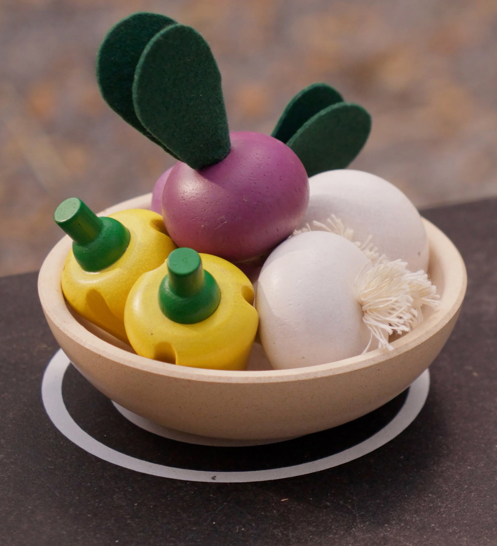 Bowl in a play kitchen filled with vegetable play food from the PlanToys wooden produce set - yellow peppers, radish and garlic. 