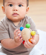A baby grasping the Plan Toys Wooden Pull & Grasp Toy.