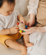 An adult handing the Plan Toys Pull & Grasp wooden baby toy to a baby.
