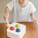 Child playing with the PlanToys punch and drop bin wooden pounding toy. Hammering the red ball into the bin through a slot on the lid.
