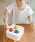 Child playing with the PlanToys punch and drop bin wooden pounding toy. Hammering the red ball into the bin through a slot on the lid.