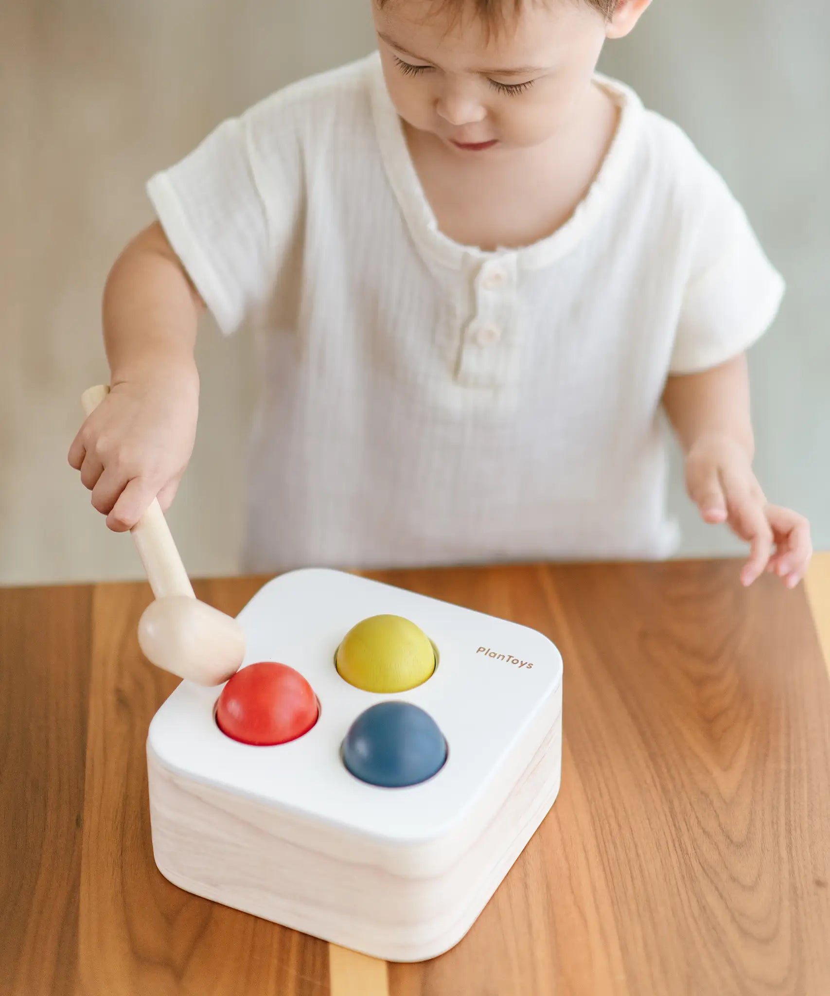 Child playing with the PlanToys punch and drop bin wooden pounding toy. Hammering the red ball into the bin through a slot on the lid.