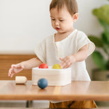 Toddler playing with the PlanToys punch and drop bin wooden pounding toy placing the coloured balls onto the frame of the box.