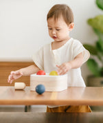 Toddler playing with the PlanToys punch and drop bin wooden pounding toy placing the coloured balls onto the frame of the box.