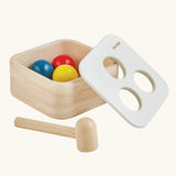 PlanToys punch and drop bin wooden pounding toy. Wooden box with three slots on the top, red, yellow and blue balls with a wooden hammer. Balls have been placed inside the box. 