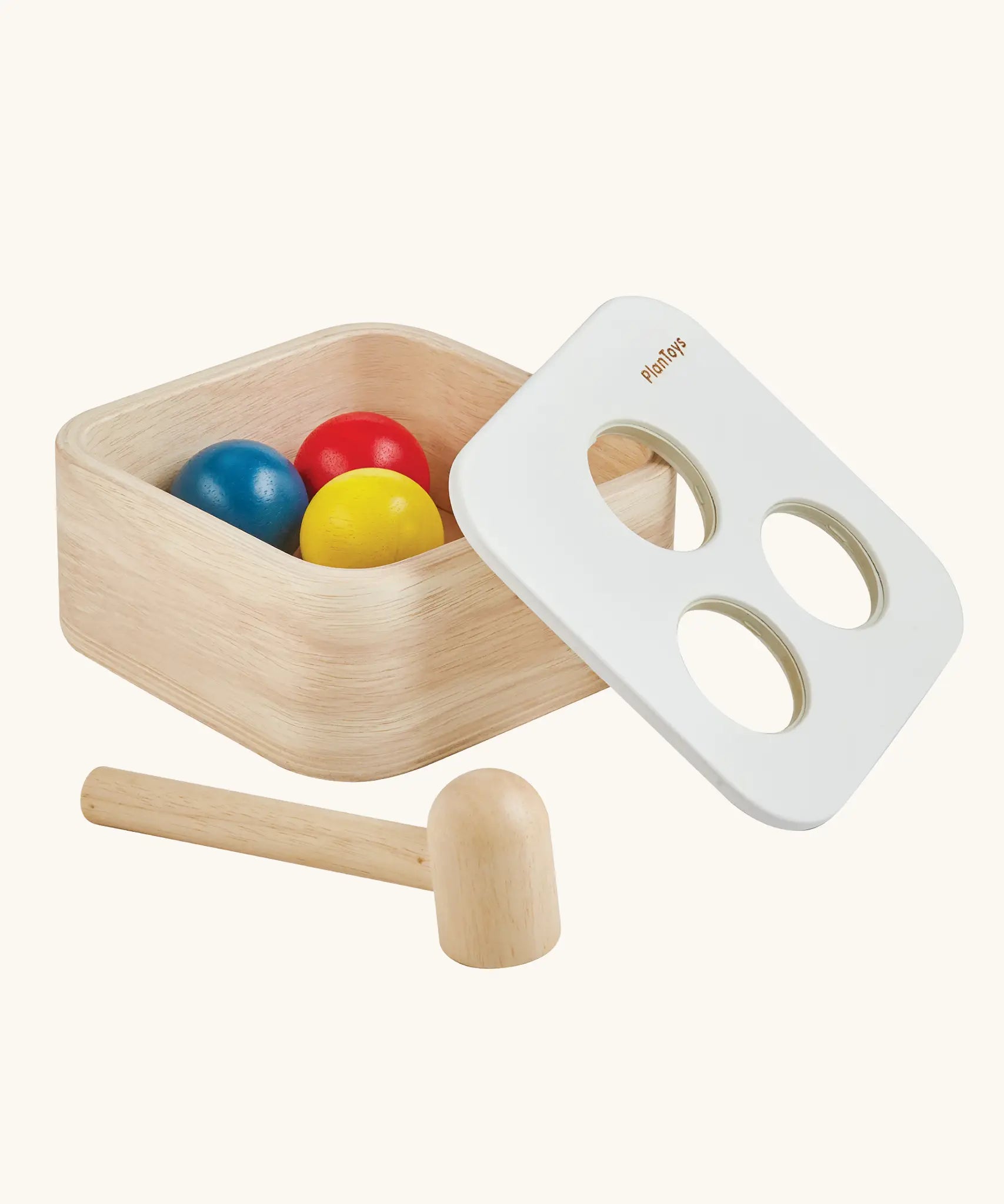 PlanToys punch and drop bin wooden pounding toy. Wooden box with three slots on the top, red, yellow and blue balls with a wooden hammer. Balls have been placed inside the box. 