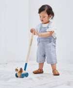Child pushing along the PlanToys push and pull puppy wooden toy with the screw in stick attached. 