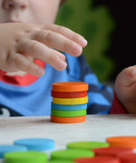 A close up of a child's hand stacking the counters from the Plan Toys Sort & Count Cups set. 