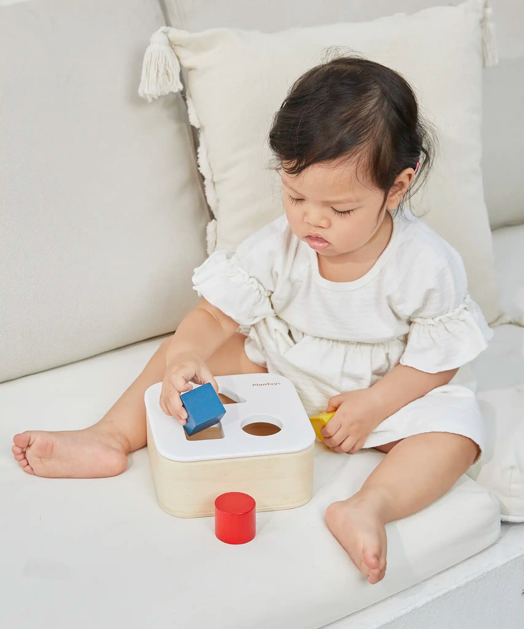 Child playing with the PlanToys shape and sort it out bin wooden shape sorter toy. 