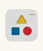 Overhead view of the PlanToys shape and sort it out bin wooden shape sorter toy. Square box with lid with three shaped holes in the lid. Yellow triangle, red cylinder and blue cube blocks.
