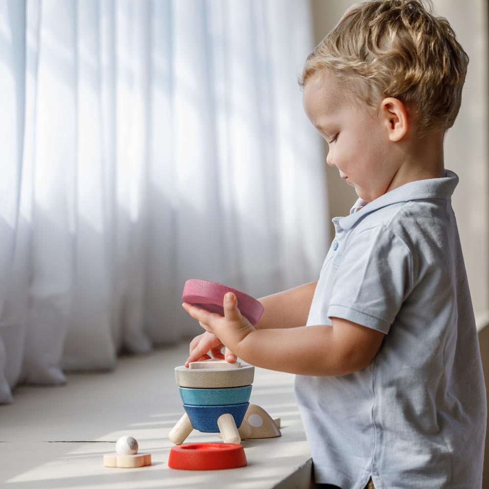 A child playing playing with the PlanToys Stacking Rocket Baby Toy, they have the pink piece in their hand. 