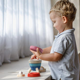 A child playing playing with the PlanToys Stacking Rocket Baby Toy, they have the pink piece in their hand. 