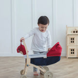 Child standing next to a PlanToys stroller with a doll house in the background