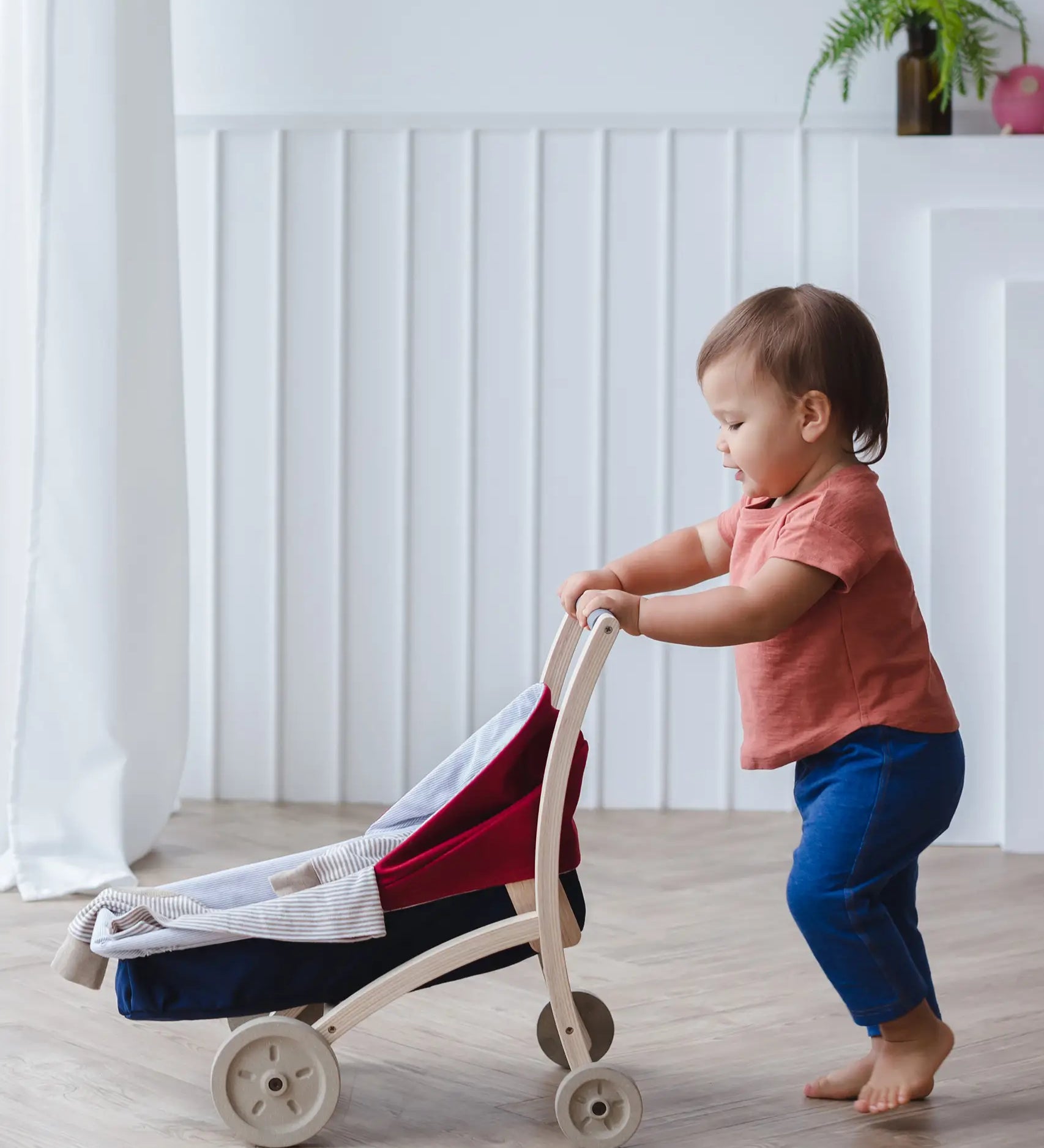 Child pushing a PlanToys stroller on a wooden floor