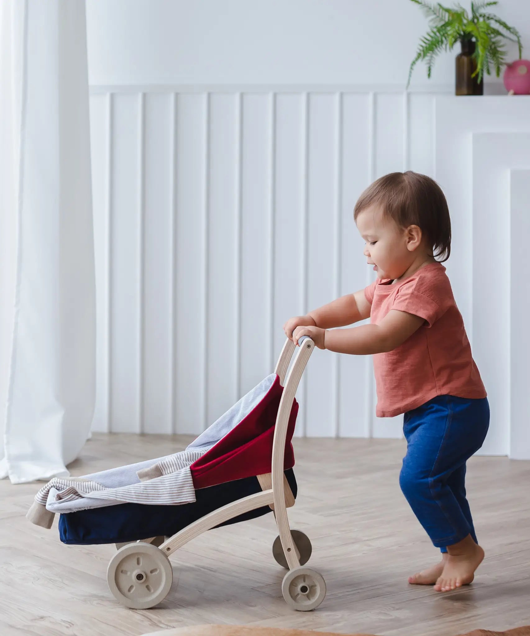Child pushing a PlanToys stroller on a wooden floor