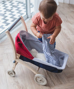Child tucking in a teddy bear in a PlanToys stroller