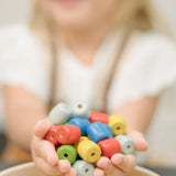 Beads from the PlanToys threading beads wooden lacing toy in a child hands. Blue, red, yellow, white and green  wooden beads.