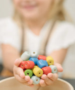 Beads from the PlanToys threading beads wooden lacing toy in a child hands. Blue, red, yellow, white and green  wooden beads.