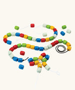 PlanToys threading beads wooden lacing toy. Rainbow coloured wooden beads threaded onto black and white laces.