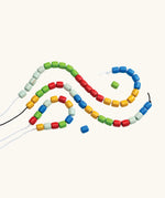 PlanToys threading beads wooden lacing toy. Rainbow coloured wooden beads threaded onto black and white laces.
