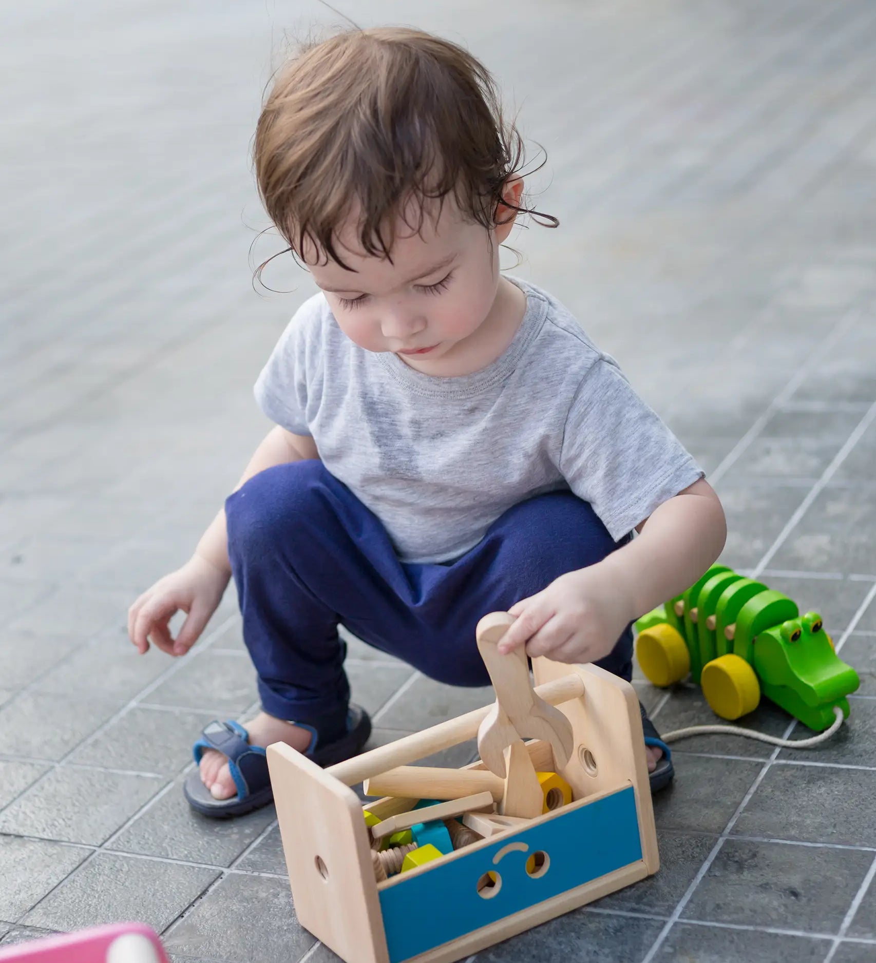 Child putting away wooden tolls and screws inside the PlanToys tool box play set
